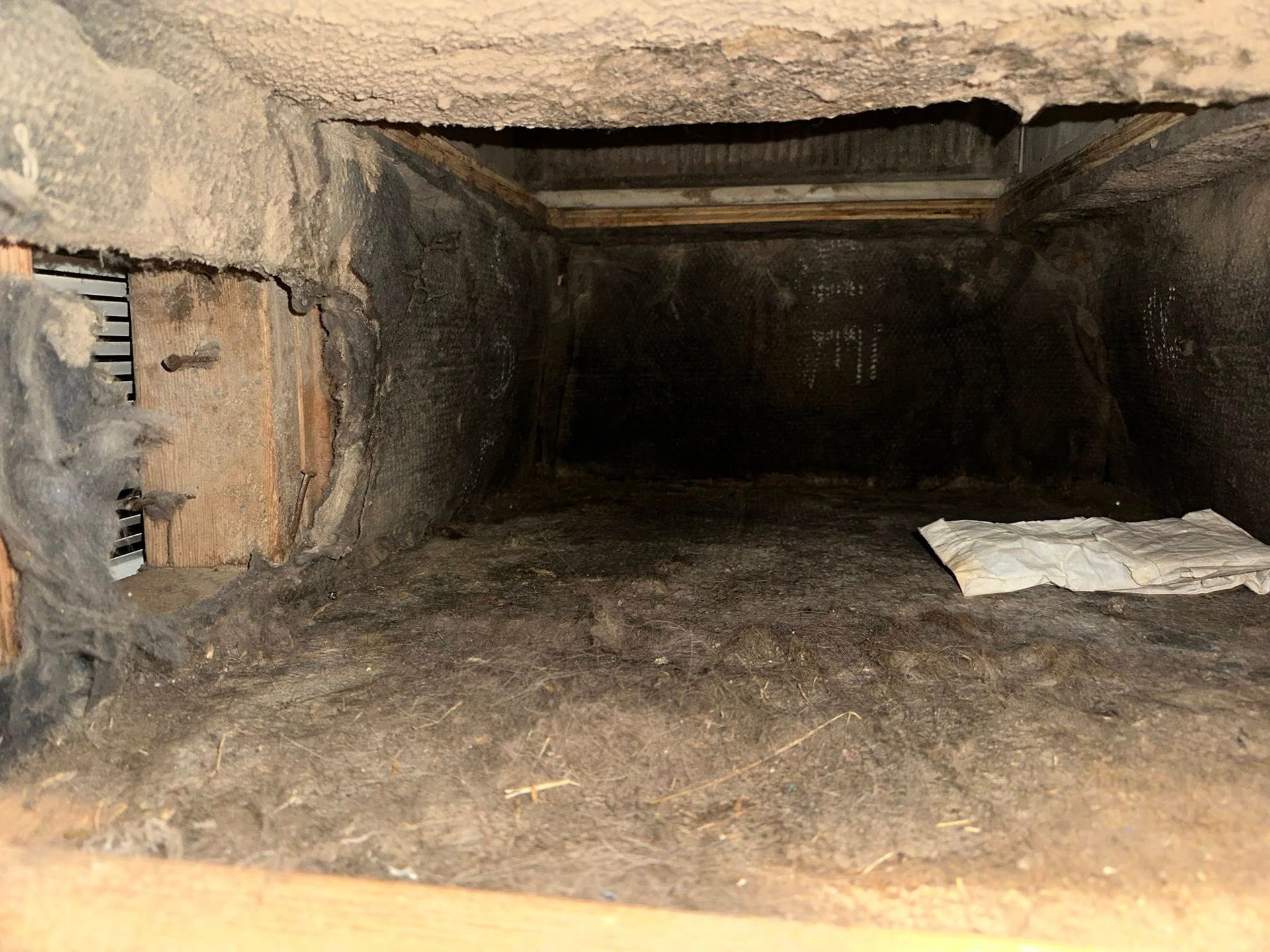 Inside of a dirty air duct, covered in dust and debris.