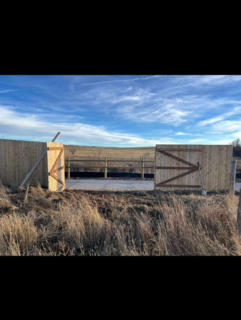 Wooden fenced enclosure with open gate in a dry field under a blue sky