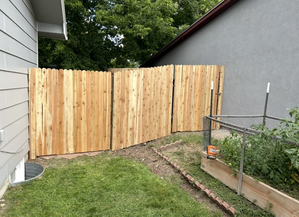 New wooden privacy fence along a narrow yard beside a house and garden bed