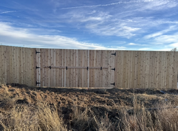 Wooden fence with a central gate under a blue sky, with dry grass in the foreground.