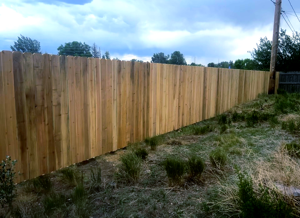 Wooden privacy fence along a grassy slope under a partly cloudy sky