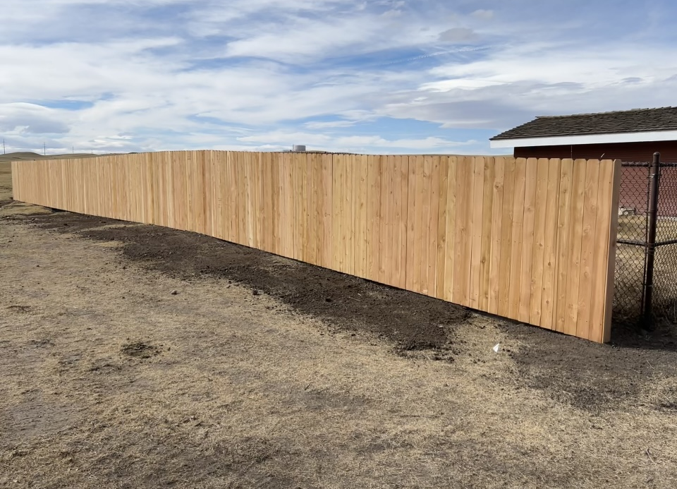 Long wooden fence along a dirt lot under a cloudy sky
