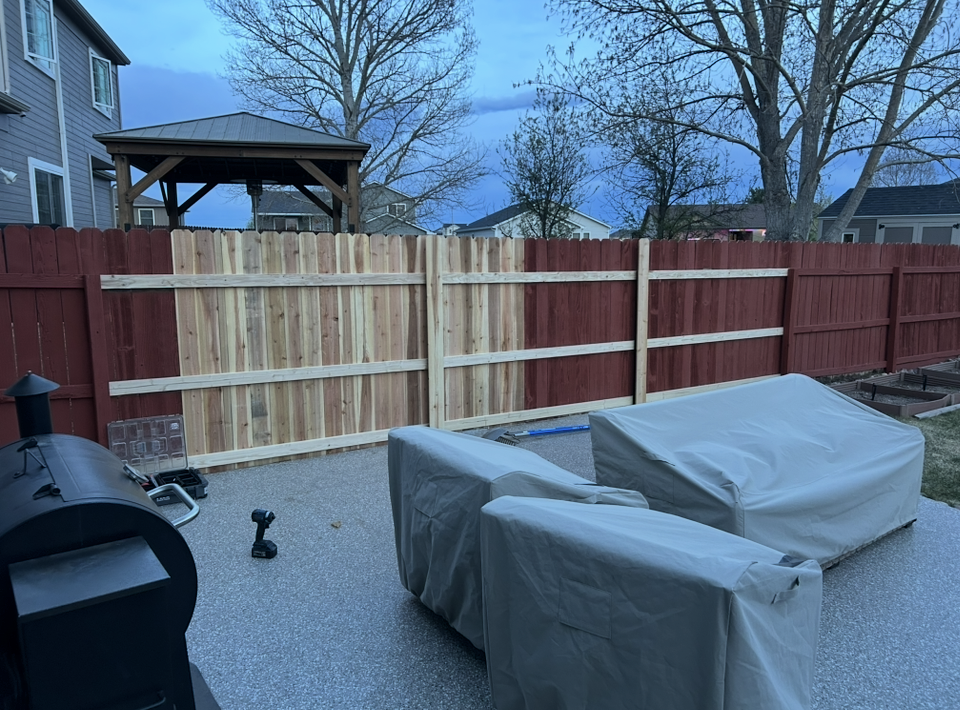 Covered patio with grill, patio furniture, and a wooden fence at dusk
