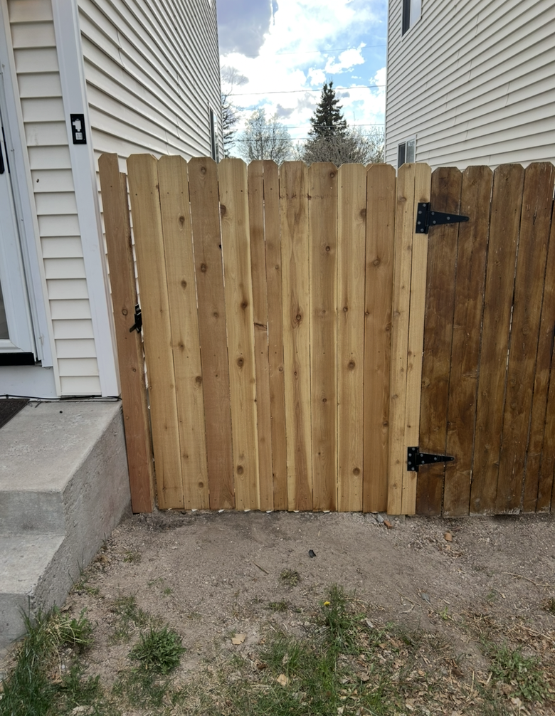 Wooden gate between two houses, with black hinges and gravel ground in front.