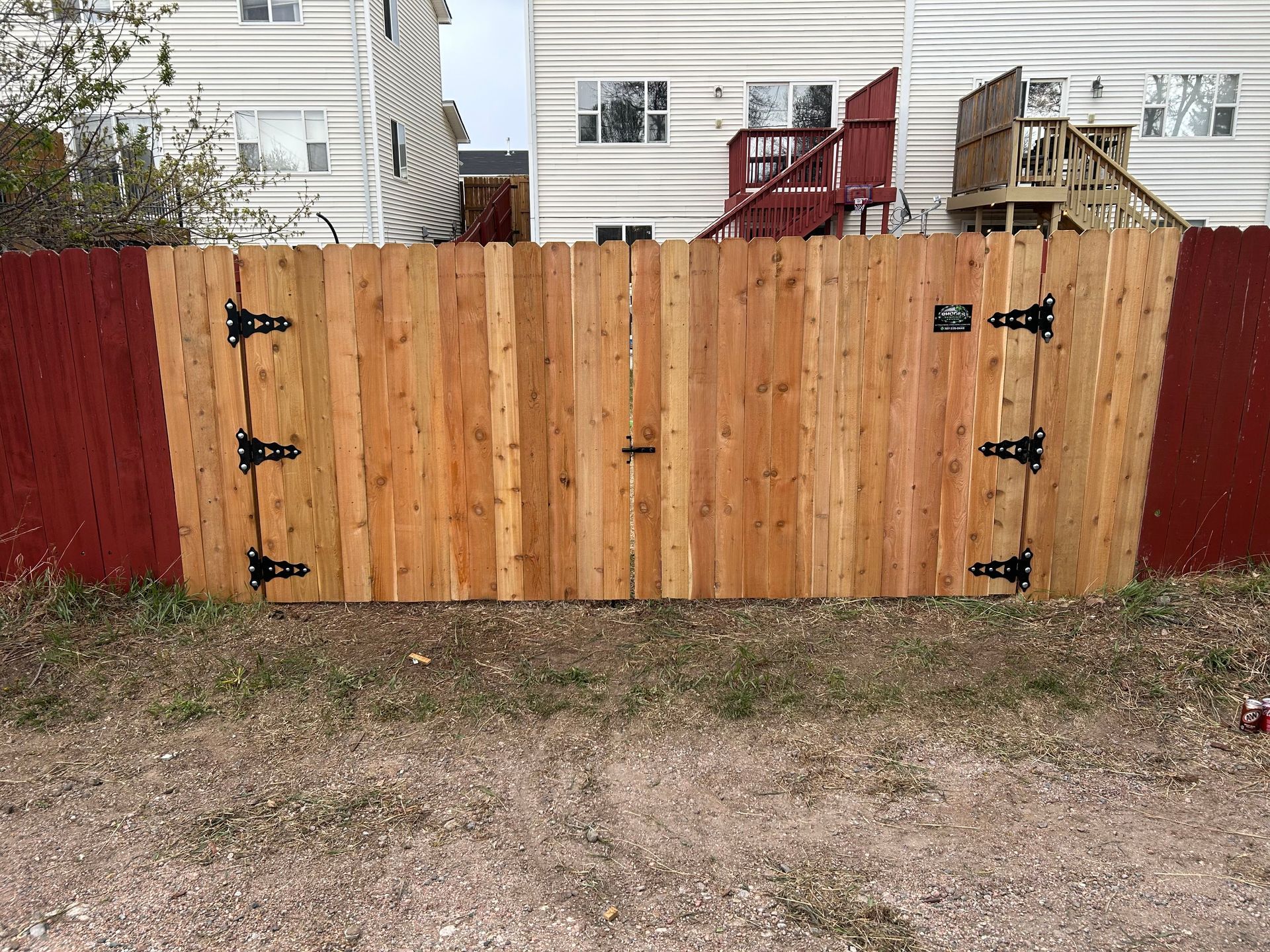 Wooden backyard fence with black hinges and red side panels in front of a house