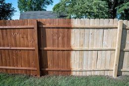 Wooden backyard fence with a dark-stained section beside a lighter weathered section under blue sky.