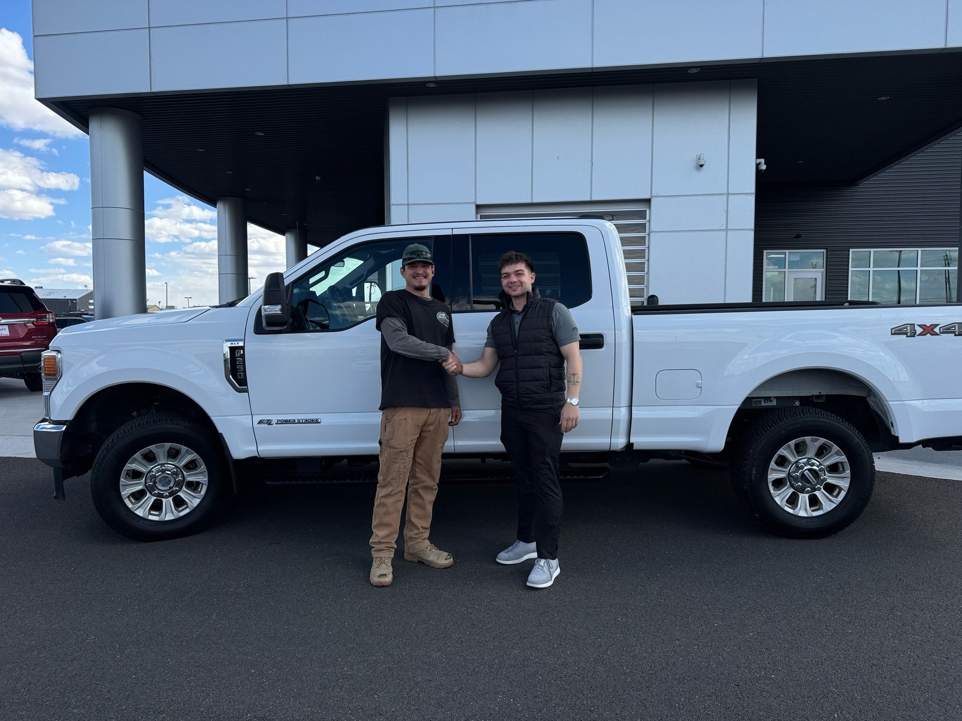 Two people standing beside a white pickup truck outside a building, shaking hands.