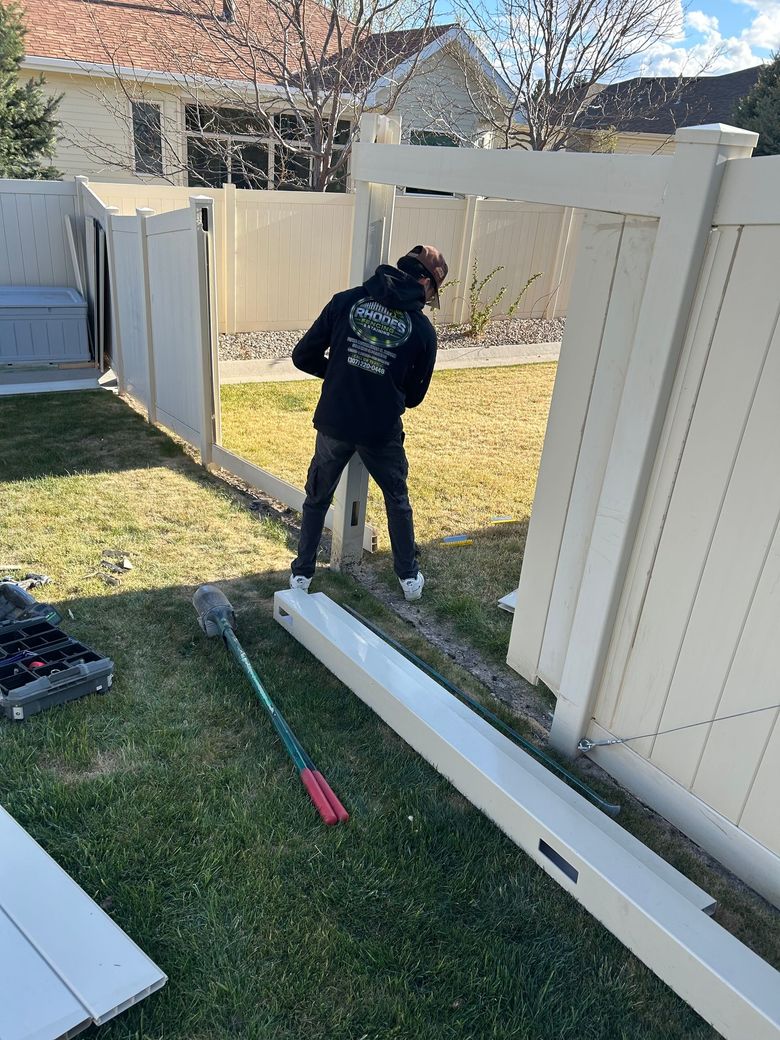 Person working on a white fence in a grassy backyard, with tools on the ground.