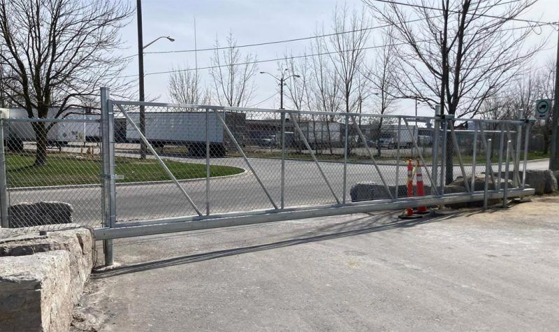 Chain-link sliding gate across a driveway with trees and industrial buildings in the background