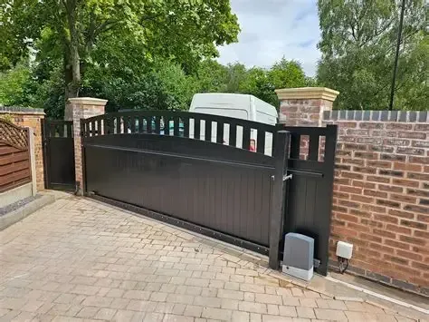 Black driveway gate between brick walls with a small gate opener at the bottom right