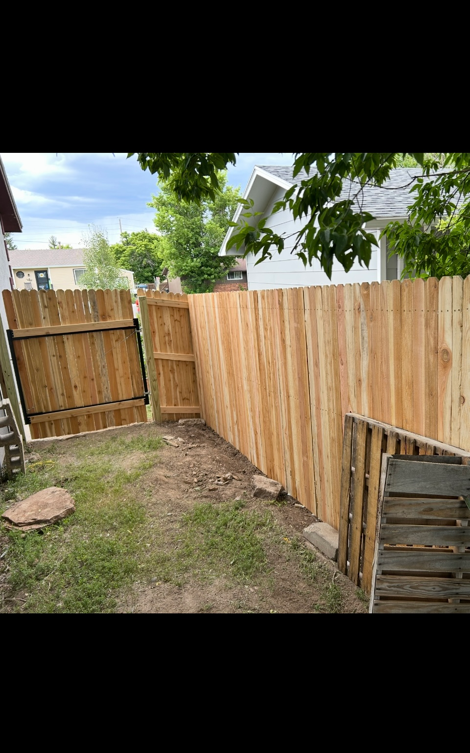 Backyard with a wooden fence, gate, patchy grass, and a leaning shed panel in the corner