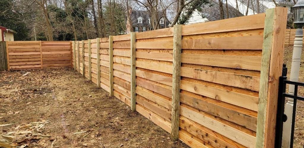 Wooden privacy fence along a dirt path in a wooded yard