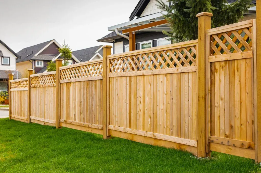 Wooden privacy fence with lattice top along a green lawn in a suburban neighborhood