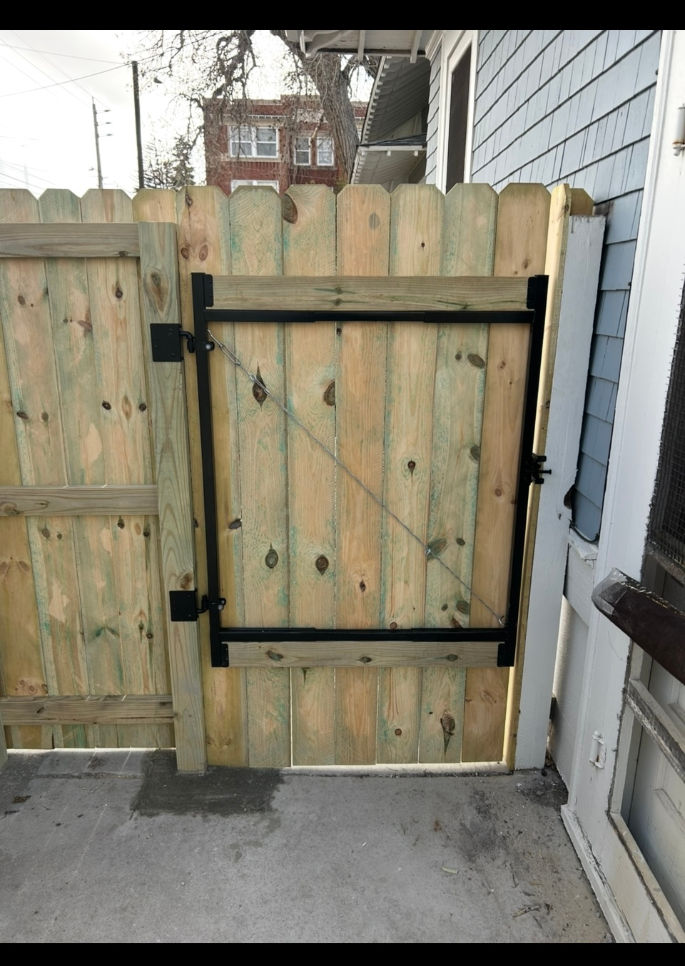Wooden backyard gate with black metal braces in a fenced outdoor area