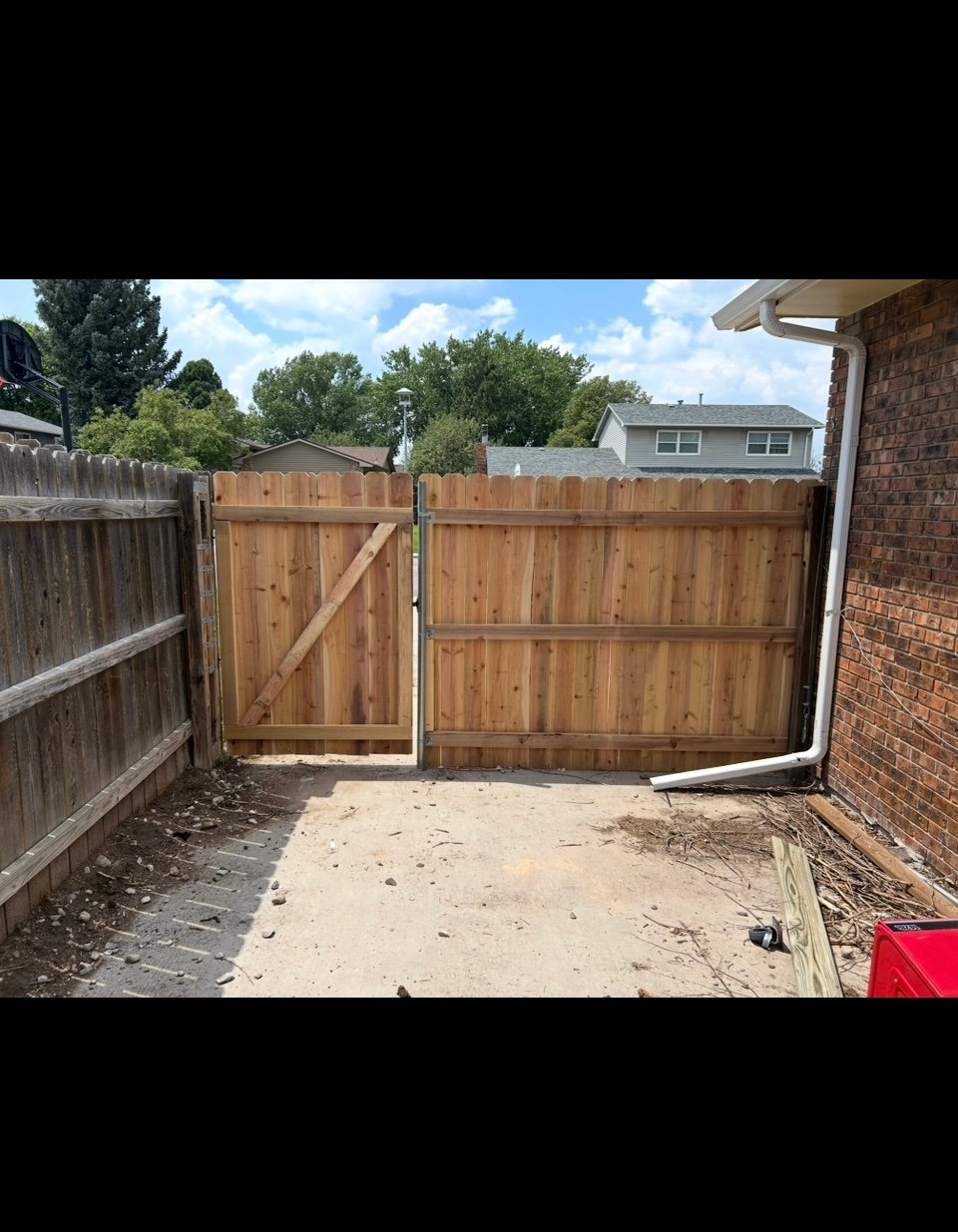 Backyard patio with a wooden privacy fence and gate, bordered by a brick house and concrete slab.