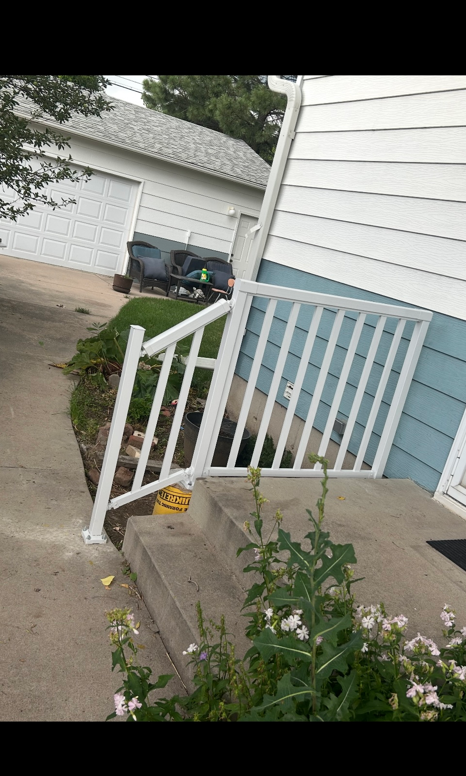 Concrete porch with white railings beside blue siding, a driveway and garage in the background.