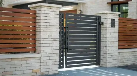 Modern house entrance with stone pillars, dark metal gate, and horizontal wooden slat fence.