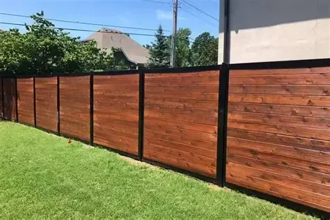 Wooden privacy fence with black posts along a grassy yard under a blue sky