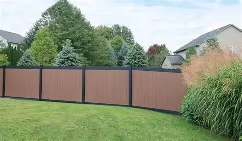 Brown privacy fence along a grassy backyard with trees and shrubs behind it