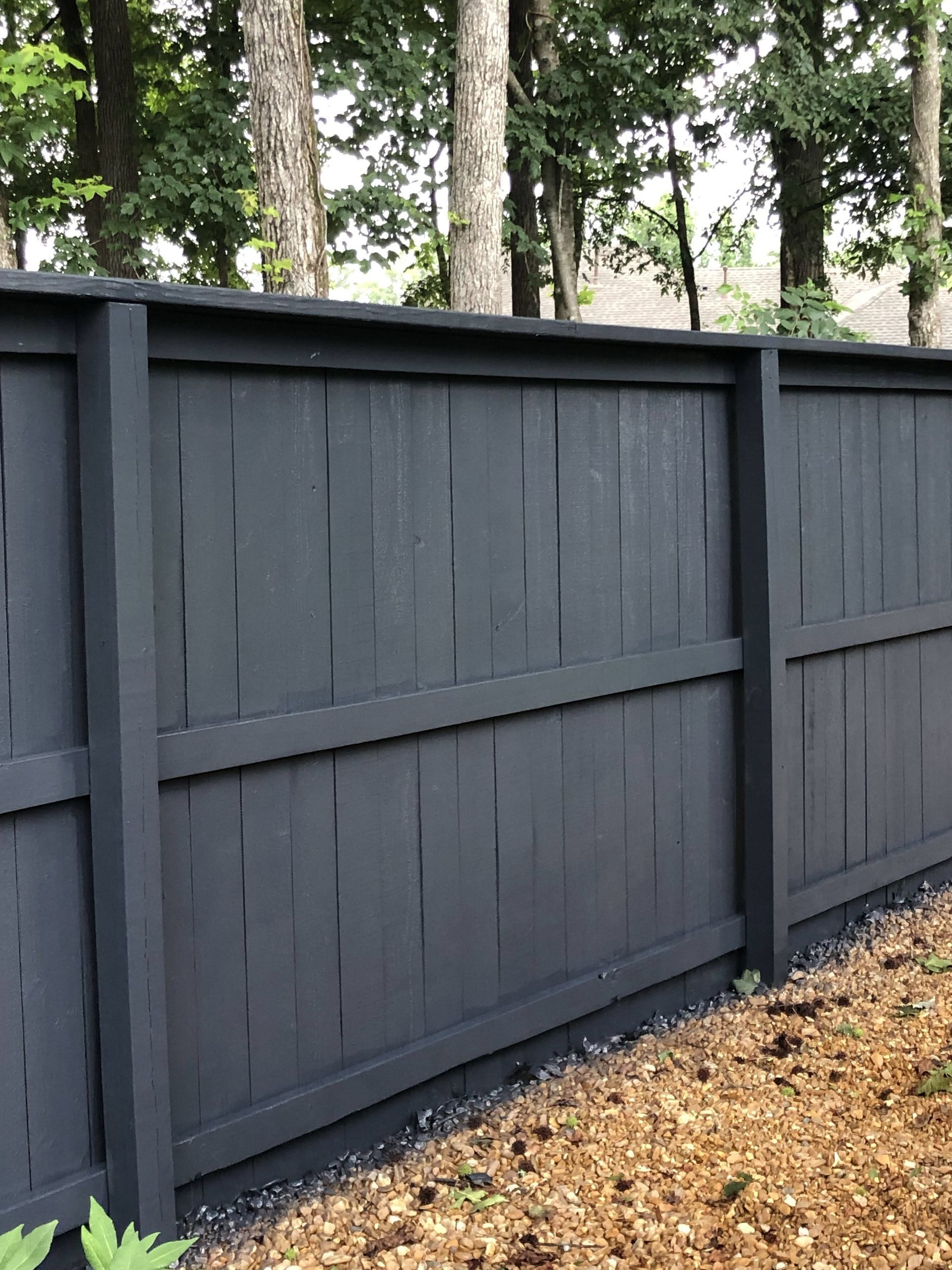 Dark gray wooden fence along a leaf-covered path with trees behind it