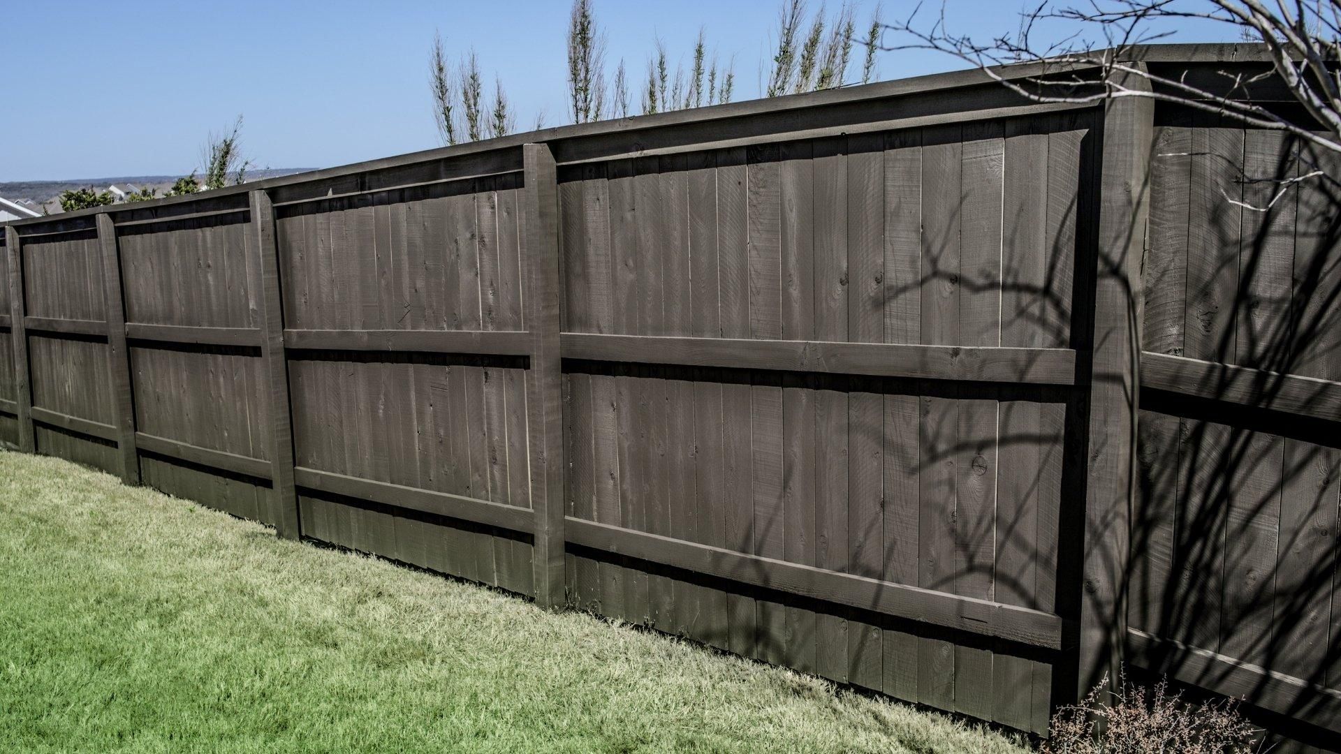 Wooden privacy fence along a grassy yard under a clear blue sky.