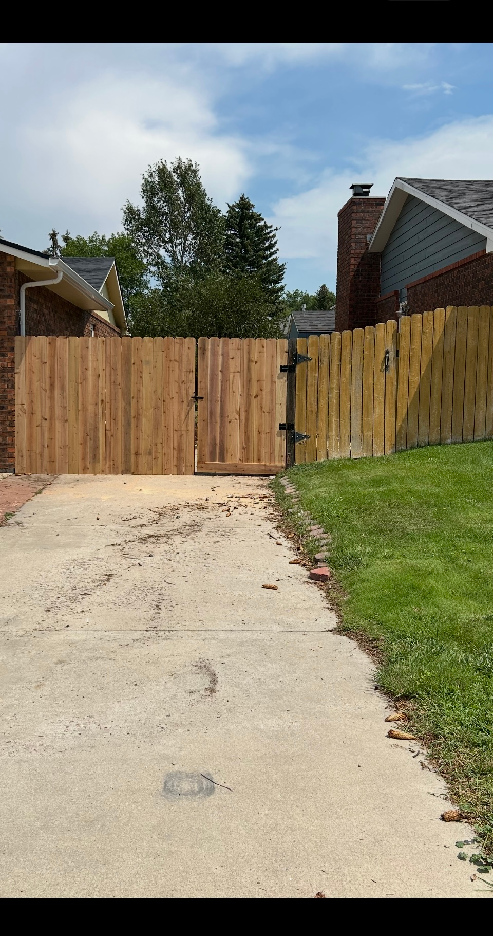 Driveway ending at a wooden fence gate beside a grassy yard and a brick house.