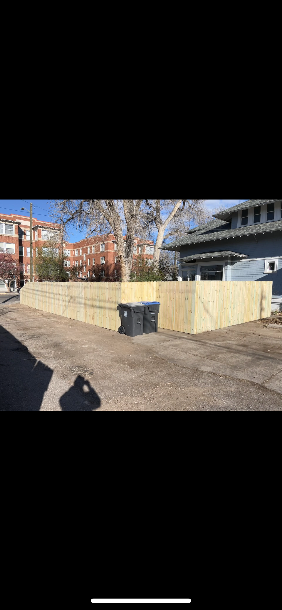 Large beige retaining wall under construction beside a dirt lot with a building in the background.