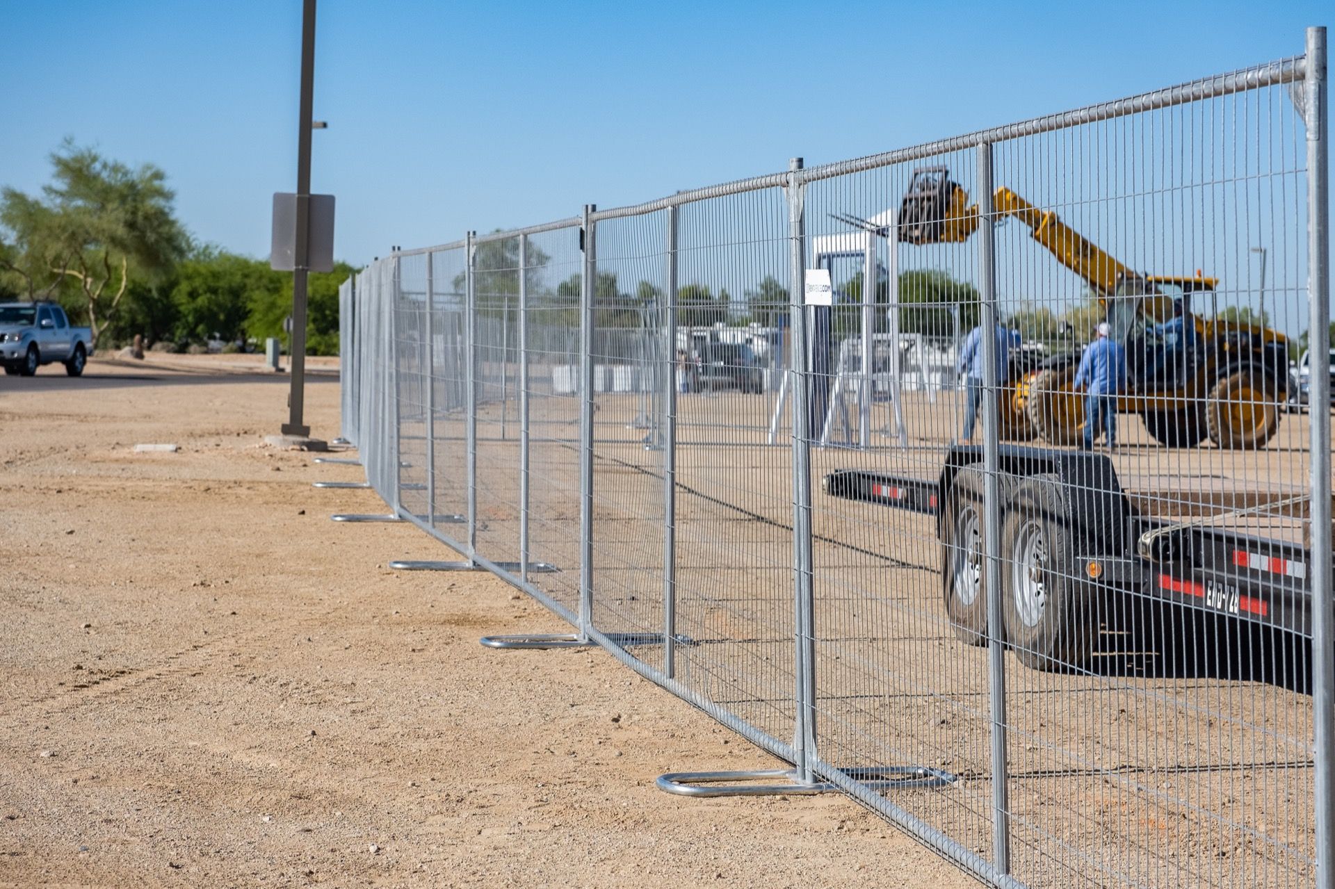 Temporary metal fence panels on a gravel lot with construction vehicles in the background.