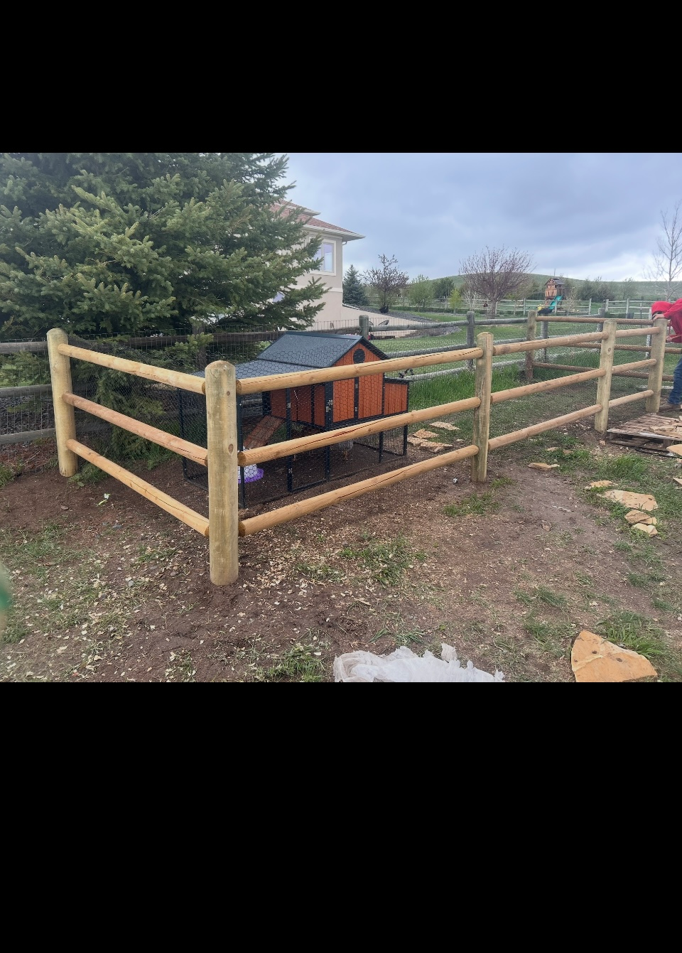 Wooden fenced enclosure around a black-and-orange object in a grassy yard