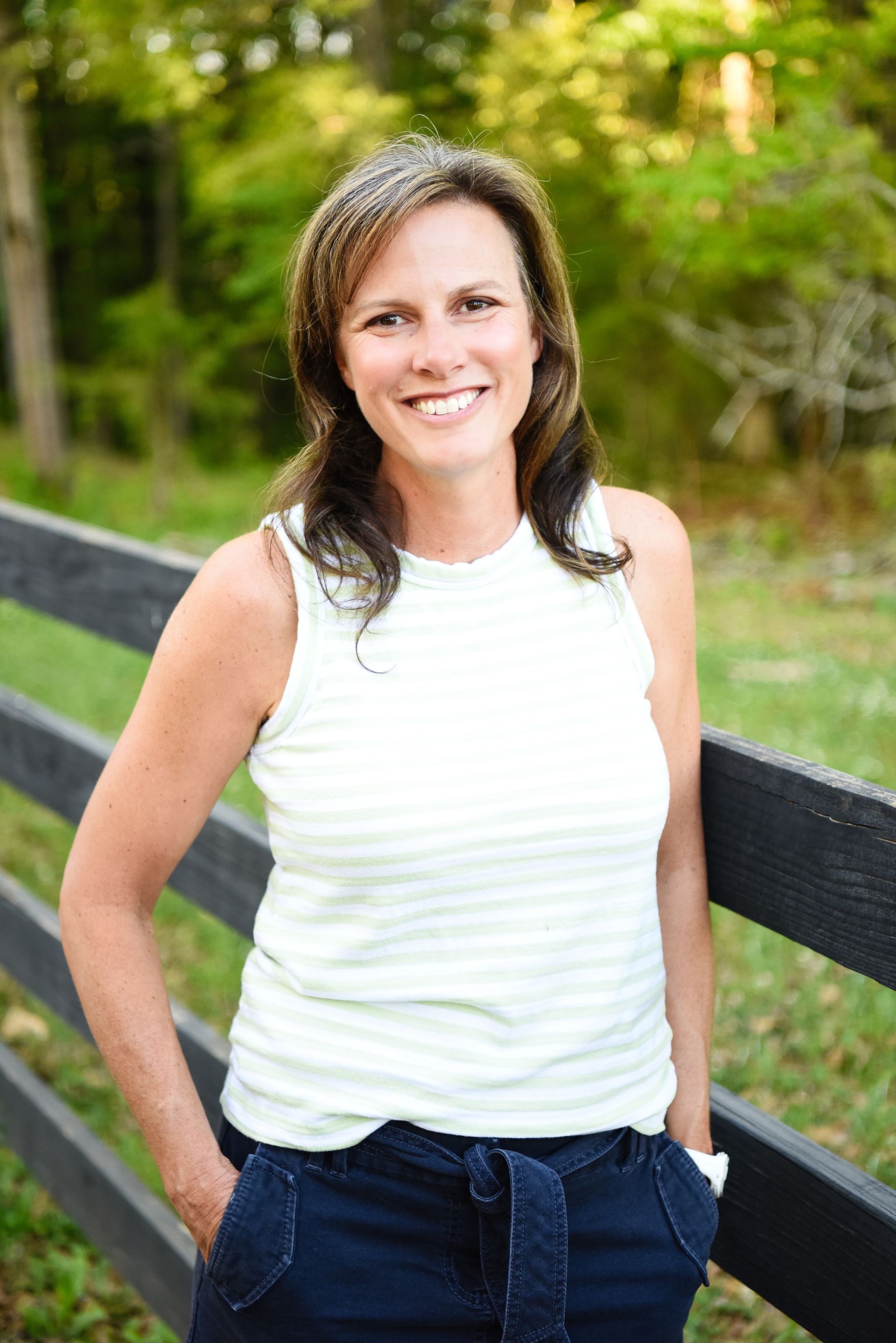 A professional in a white medical coat standing outdoors with arms crossed, smiling at the camera.