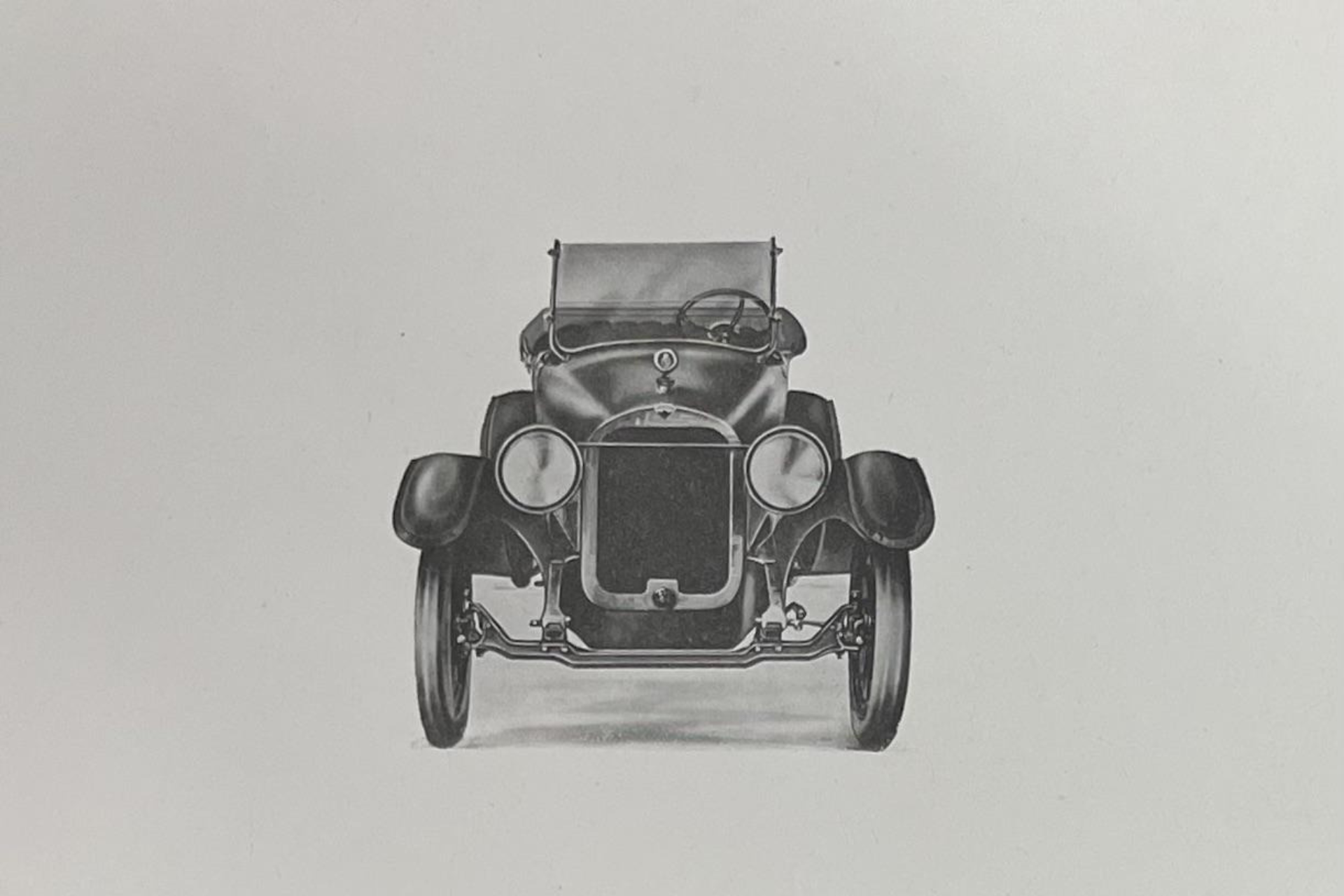 A black-and-white, front-facing view of a vintage, open-top automobile on a light background.