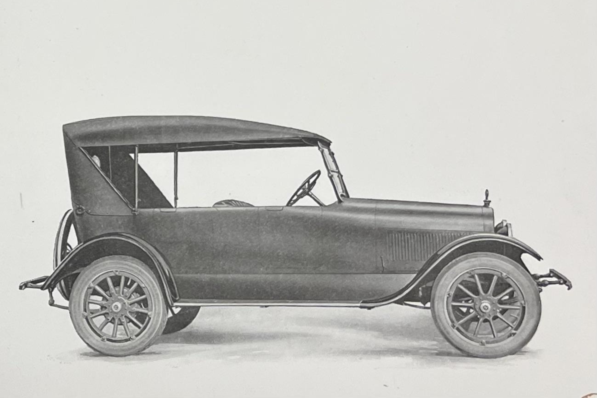 A side-profile view of a black antique, open-top touring car with spoked wheels against a plain white background.