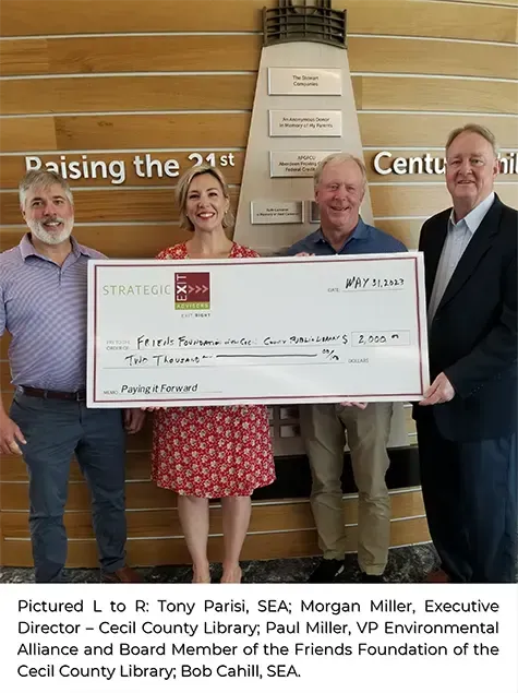 Four people holding a large check in front of a wall with text.