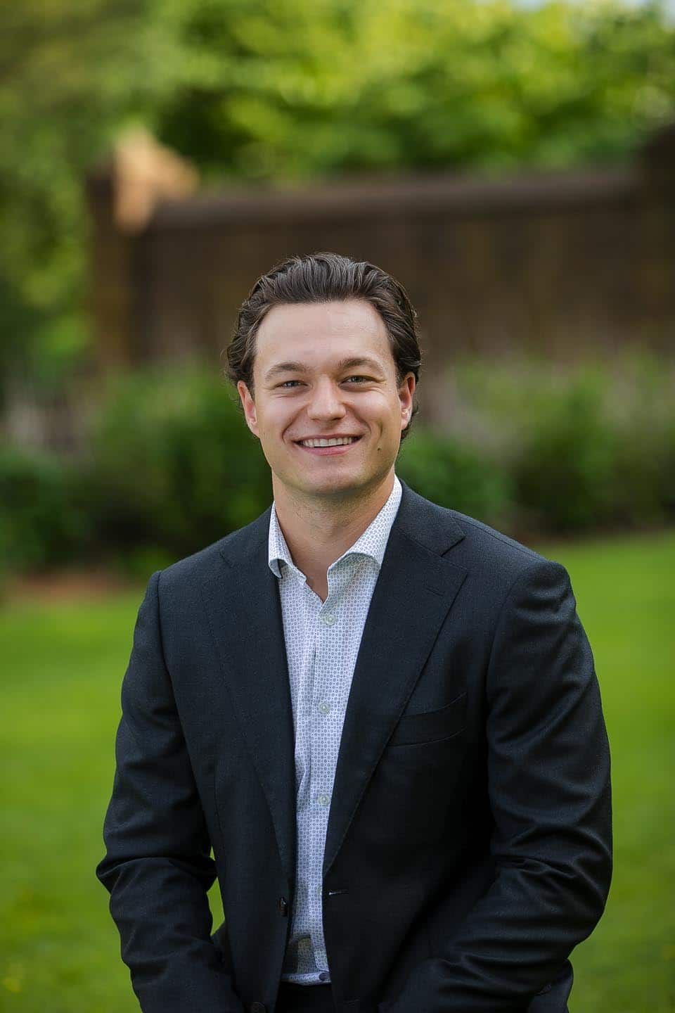 Man in suit smiles outdoors.