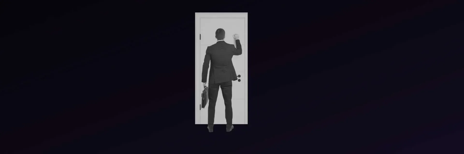 Man in a suit standing in a doorway, raising a hand.