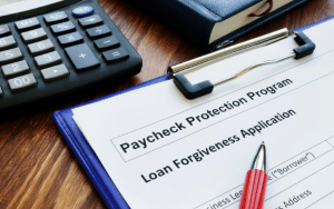 Paycheck Protection Program loan forgiveness application on clipboard next to calculator and pen.