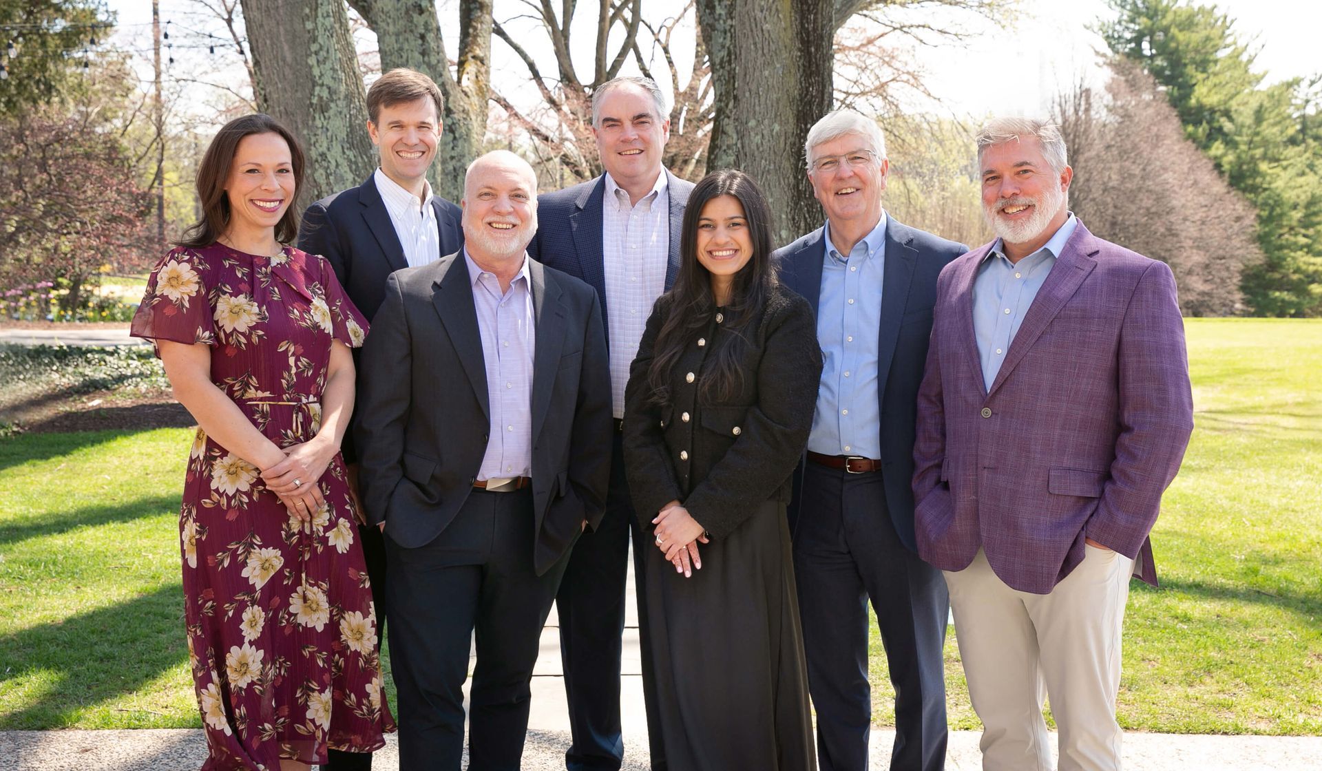 Group of people, business attire, pose outdoors in front of a brick building.