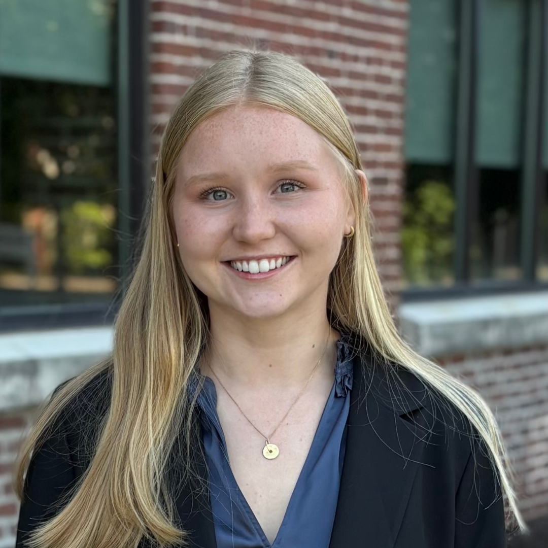 Smiling blonde person standing outdoors in front of a brick building