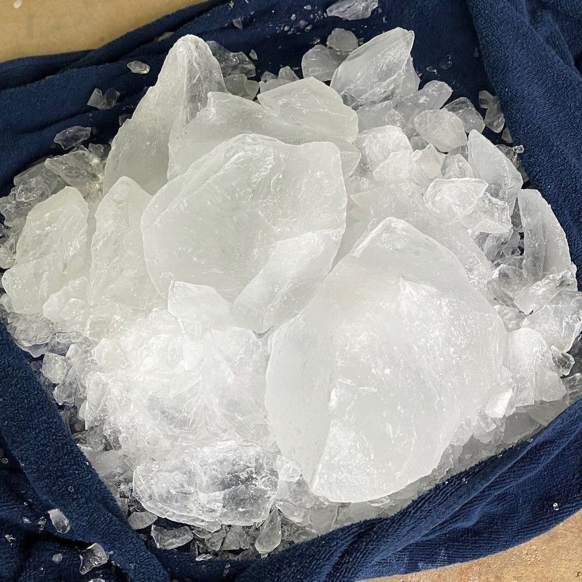 Pile of clear, crystalline ice chunks on a folded blue cloth, reflecting light.