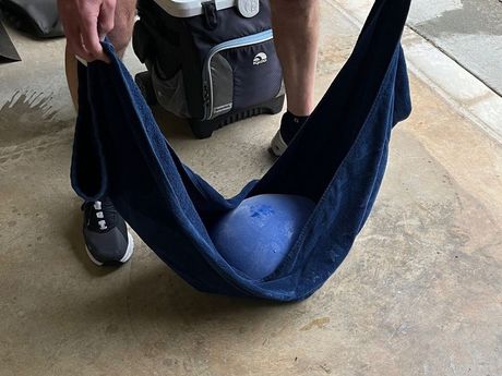 Person holds a blue towel, forming a hammock holding a large, blue ice ball outside.