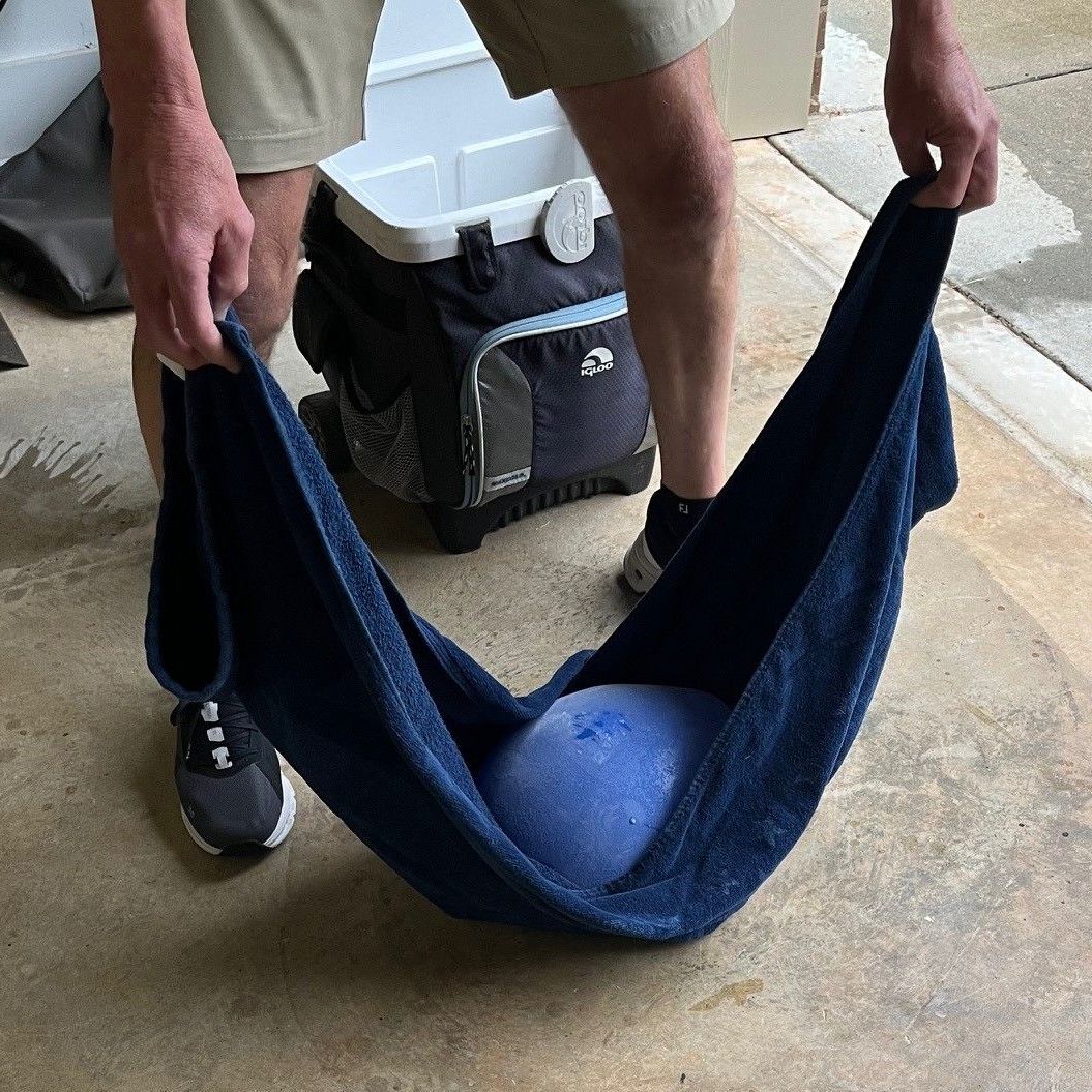 Person holding a blue ball in a dark blue towel, outdoors near a cooler.