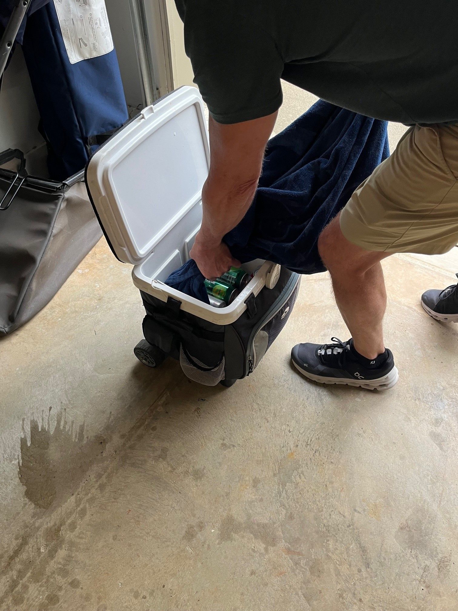 Person reaching into a cooler containing items; outdoors.