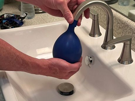 Person filling a blue balloon with water from a bathroom sink faucet.