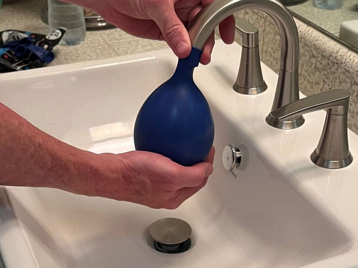 Person filling a blue balloon with water at a bathroom sink.