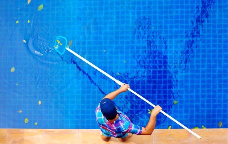 Person cleaning a blue tiled pool wall with a long-handled brush underwater