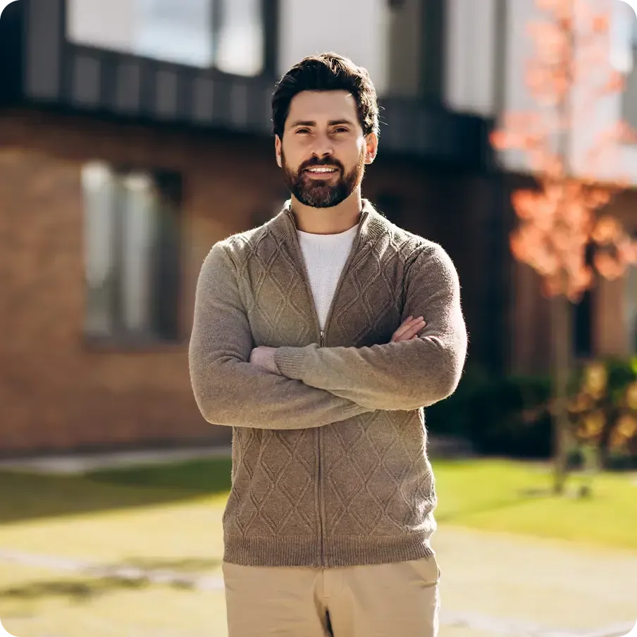 Happy handsome man businessman posing in front of modern suburban house looking at camera.