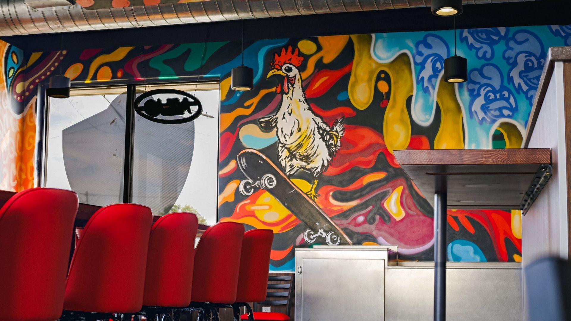 Colorful mural of a chicken skateboarding inside a restaurant, red chairs line the counter.