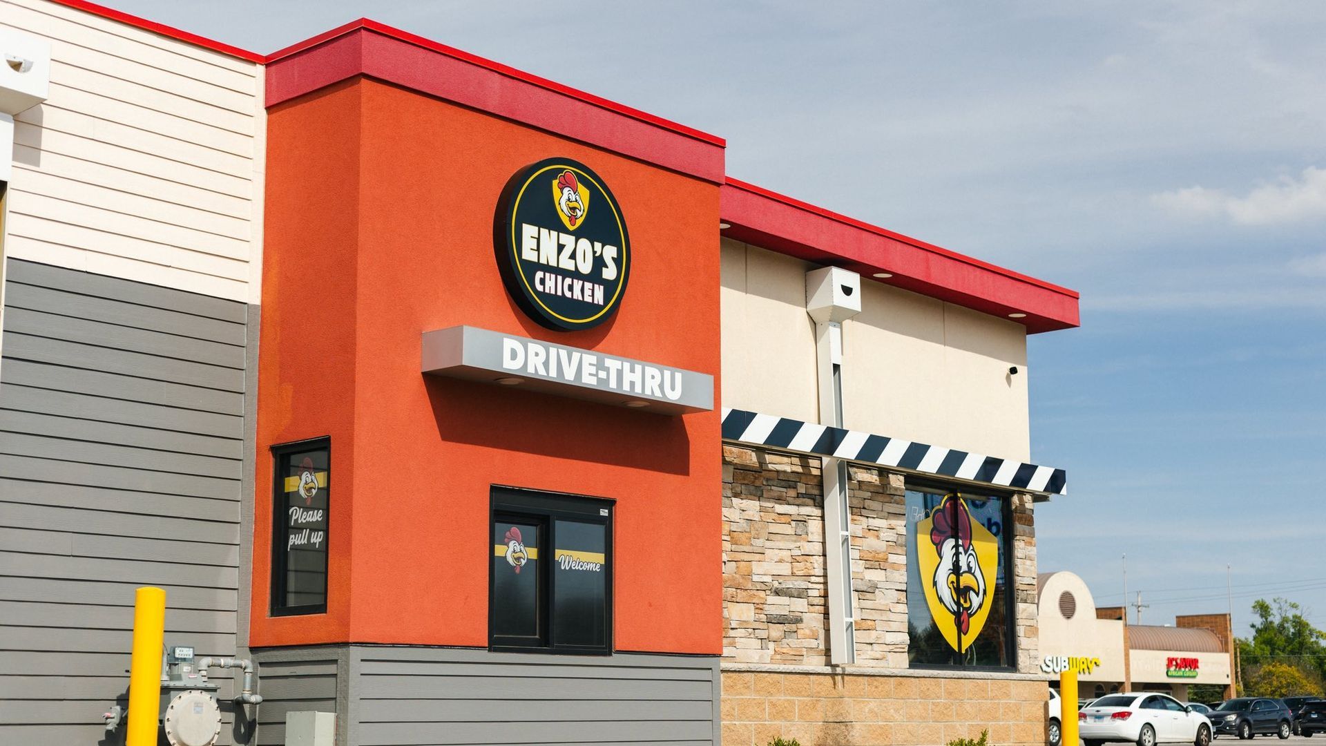Enzo's Chicken restaurant with drive-thru. Orange, red, and beige building with black and yellow signage, clear sky.