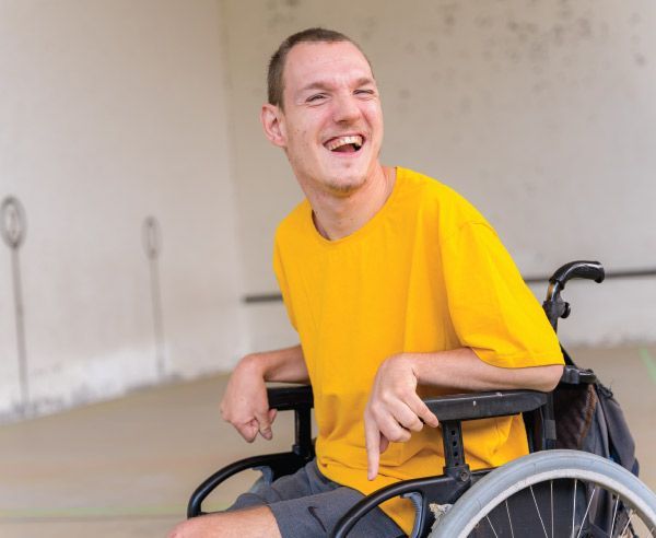 A man in a yellow shirt is sitting in a wheelchair and smiling.