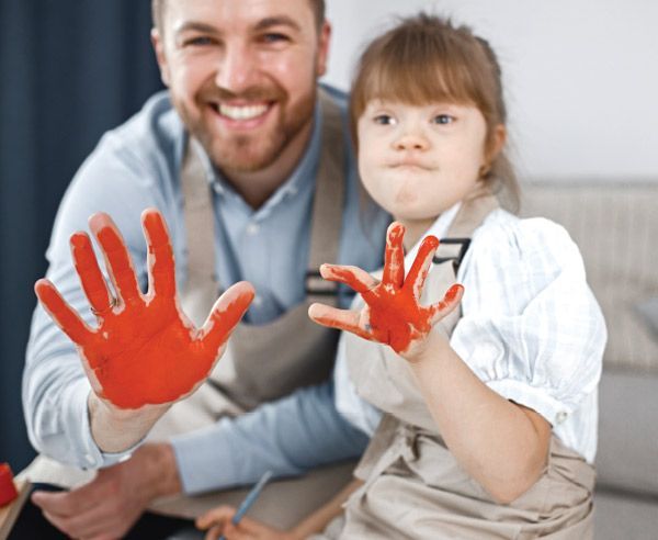 A man and a little girl are playing with red paint on their hands.